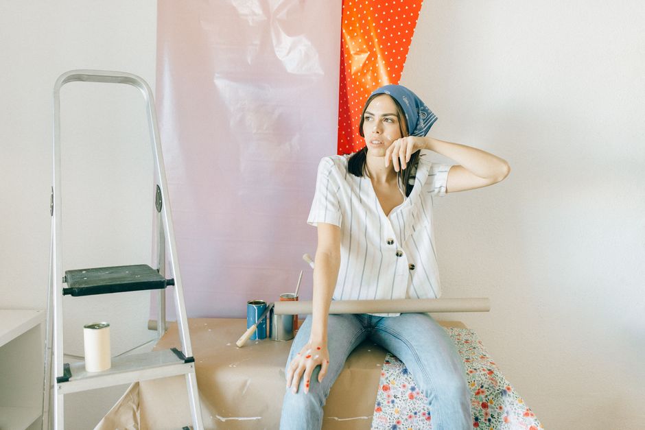 A woman sitting indoors with wallpaper and ladder, planning home renovation.
