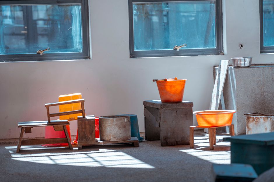 Artistic still life of wooden stools and plastic buckets in a rustic indoor setting.
